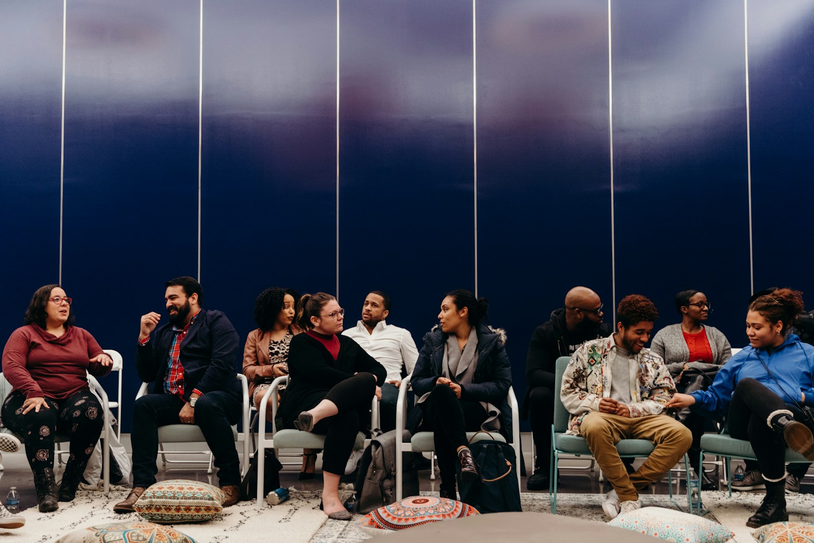 A diverse support group seated in a circle of chairs, talking together in a bright room.